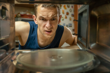 Dark-haired man has opened the microwave oven and looks at it with a surprised look, a photo from inside.