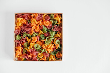 Multicolored pasta in a cardboard box on a white background. Top view. Copy, empty space for text