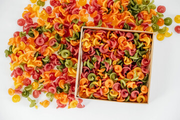 Multicolored pasta in a cardboard box scattered on a white background. Top view. Copy, empty space for text