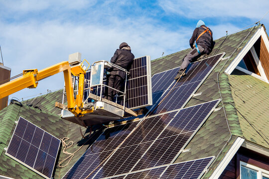Workers installing solar panels on private home hexagonal roof felt on sunny day, blue sky. Real life. Home power plant.