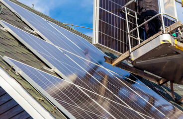 Workers installing solar panels on private home hexagonal roof felt on sunny day, blue sky. Real...
