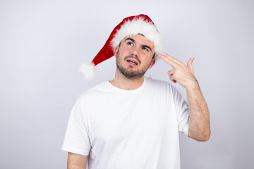 Young handsome man wearing a Santa hat over white background Shooting and killing oneself pointing hand and fingers to head like gun, suicide gesture.