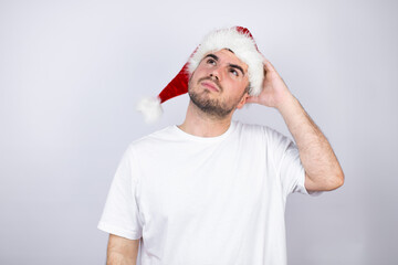 Young handsome man wearing a Santa hat over white background putting one hand on her head smiling like she had forgotten something