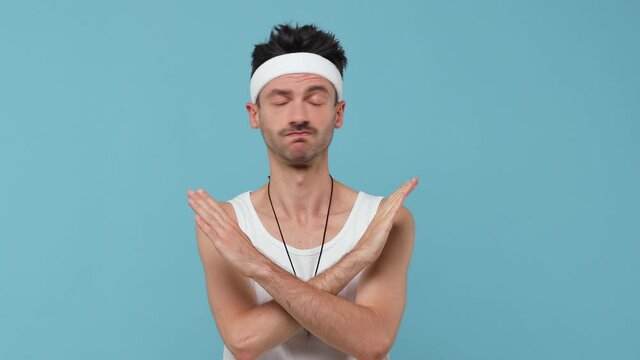 Dissatisfied young fitness man with thin skinny body sportsman in headband shirt isolated on blue background. Workout gym sport motivation concept. Showing stop gesture with palm crossed hands say no