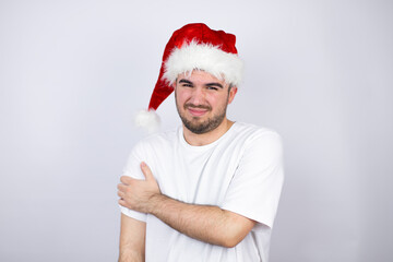 Young handsome man wearing a Santa hat over white background with pain on her shoulder and a painful expression