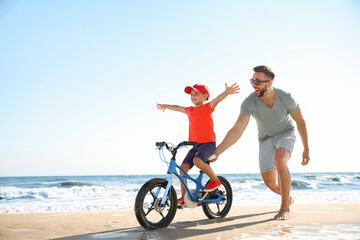 Fototapeta na wymiar Happy father teaching son to ride bicycle on sandy beach near sea