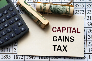 CAPITAL GAINS TAX words on a white sheet against a table with numbers, banknotes and calculator