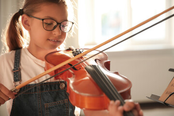 Cute little girl playing violin indoors, closeup. Music lesson