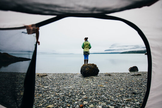 View through camping tent doorway of woman standing on beach,an inlet on the Alaska coastline. 