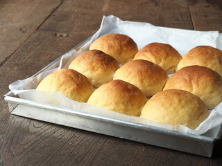 Freshly baked bread buns in baking tin on wooden table