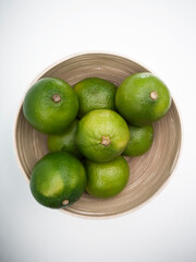 Top view of bowl with green limes and mint leafs inside on the white background. Juicy colorful fruits for mojito. Freshness and health.