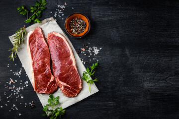 Raw beef steaks and spices for cooking them on a black background, top view, free space for text