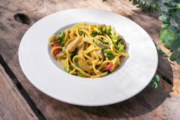 Green curry spaghetti with chicken in a white plate placed on a wooden table.