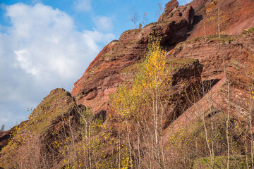Red mountains with autumn trees and blue cloudy sky. Colored waste heaps after extracting coal from...