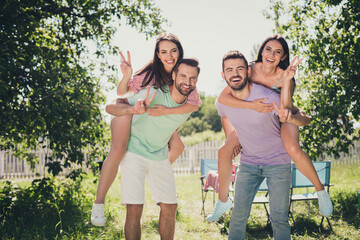 Obraz premium Photo of two couples fellows sitting piggyback showing v-sign outdoors outside backyard forest countryside