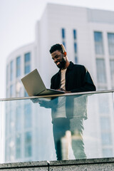 Communication Concept. Portrait of african man talking on smart phone and using laptop in the street