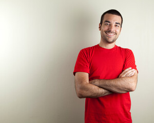 Studio photo of smiling man in his 30s with crossed arms wearing a red t shirt. Isolated on bright...