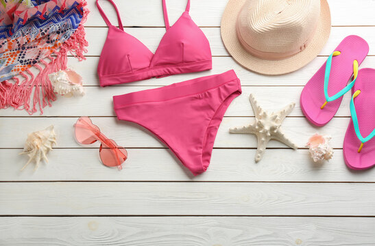 Beautiful pink bikini and beach accessories on white wooden background, flat lay