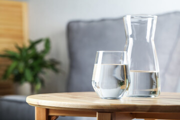 Jug and glass of water on wooden table in room, space for text. Refreshing drink