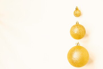 Three golden Christmas balls of different sizes are displayed in a row as a border on a white background. Copy space.