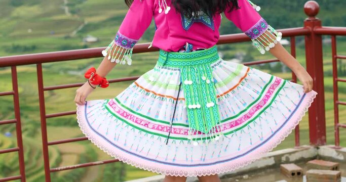 Jolly Asian girl in colorful cultural dress playfully dancing and smiling.