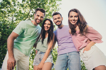 Low angle view photo of four attractive men and woman hug each other friends beaming happy smile rest in park outside in outdoors