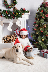 happy african american girl holding gift box while sitting with dog and cat near christmas tree and fireplace