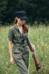 Woman on nature With weapons in hand green jumpsuit travel hunting black cap 