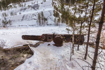 Abandoned industrial chain saw on the bottom of the quarry in winter