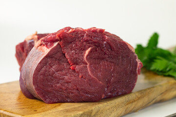 Close of view of slices fresh beef on wooden brown plate, with green celery and spring onion. White isolated background. 