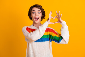 Photo of lovely funny girl raie arms fingers show heart figure open mouth wear striped sweater isolated yellow color background
