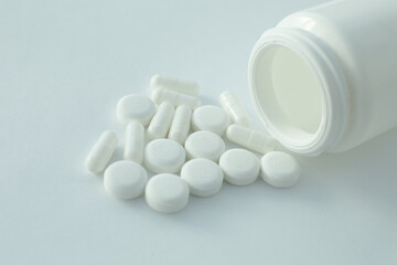 On a white background lies a plastic bottle with pills scattered nearby