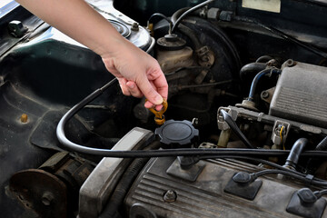 A woman checks the engine oil in an old car parked in the garage before leaving, wiping the car before traveling.