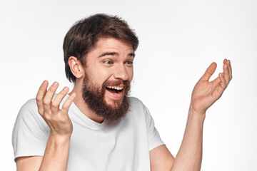 cheerful bearded man in a white t-shirt emotions gestures with his hands light background studio