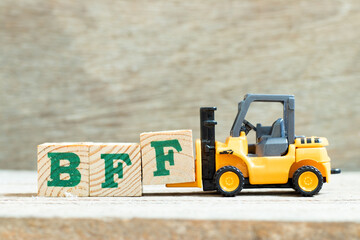 Toy forklift hold letter block f to complete word BFF (Abbreviation of best friend forever) on wood...