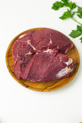 Close of view of slices fresh beef on wooden brown plate, with green celery and spring onion. White isolated background. 