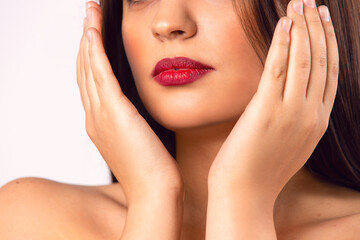 Fototapeta premium Brunette girl. Beautiful model with red lips. Hands partially covering her face. Beauty and Makeup concept