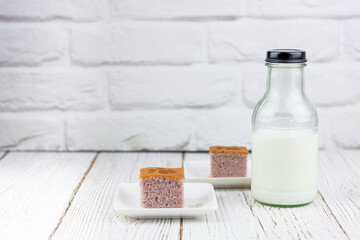 A bottle of fresh milk served with a square-cut of sweet potato cake on a white plate in the kitchen. Bakery and beverage concept.