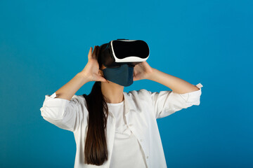 Woman in face mask wearing white shirt with VR glasses on blue background. Pandemic coronavirus. Medical mask, protection against coronavirus. 