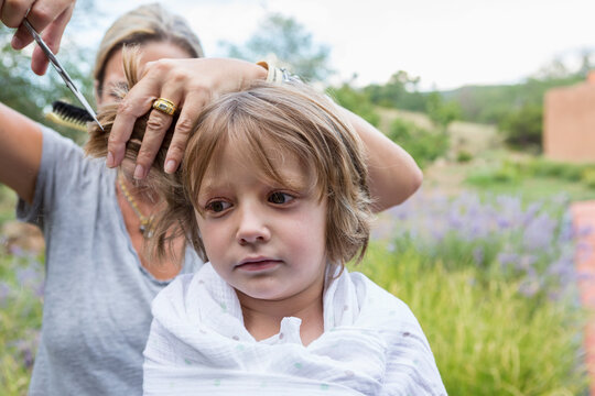 5 year old boy getting his hair cut by mother outside