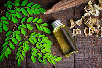 Oil of Moringa in bottle, green leaves, pods and seeds on wooden background. Moringa oleifera tropical herb product concept. 