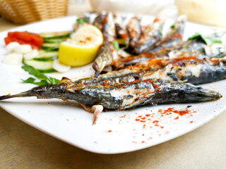 Fresh Grilled sardines served with fresh tomatoes, cucumbers slices and lemon on white plate for mediterranean healthy meal