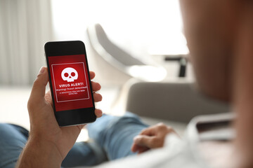 Man holding smartphone with warning about virus attack at home, closeup