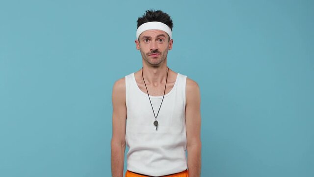 Confused puzzled young fitness man with thin skinny body sportsman in headband shirt isolated on blue background. Workout gym sport motivation concept. Looking aside spreading arms put hand on head
