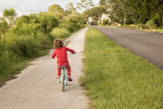A five year old boy in a red shirt riding his bike on a quiet residential street. 
