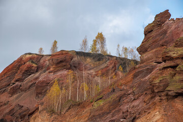 Red mountains with autumn trees and blue cloudy sky. Colored waste heaps after extracting coal from...