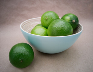 Light blue bowl with limes inside and a lime outside on craft background. Juicy, fresh and colorful fruits
