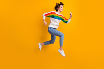 Fototapeta na wymiar Profile full size photo of positive cool girl run in air wear rainbow sweater denim jeans white sneakers isolated on yellow background