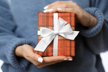 Woman in warm sweater holding Christmas gift, closeup view