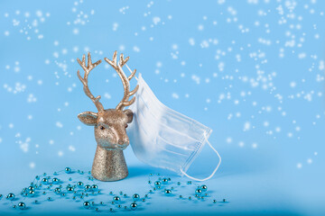 Christmas composition in minimal style. Golden deer head with medical mask on horns on blue...